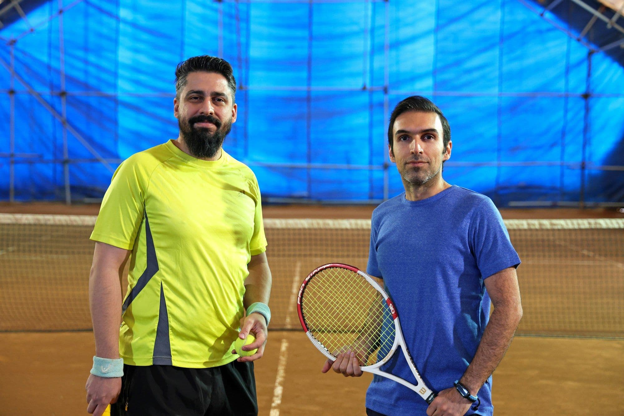 Two coaches with rackets in an indoor clay hall