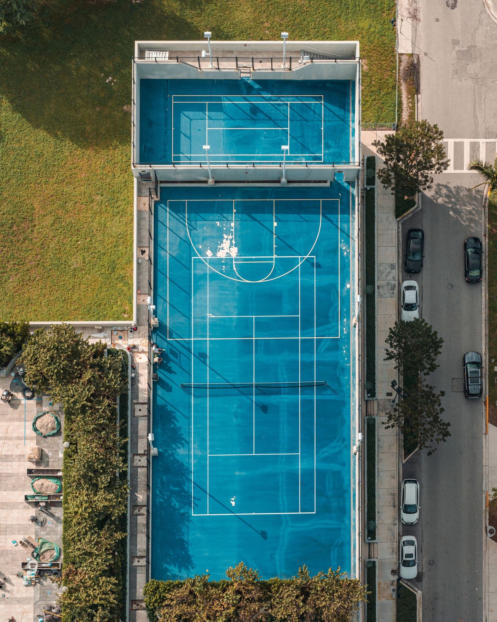 A tennis court seen from directly above, between city buildings and trees
