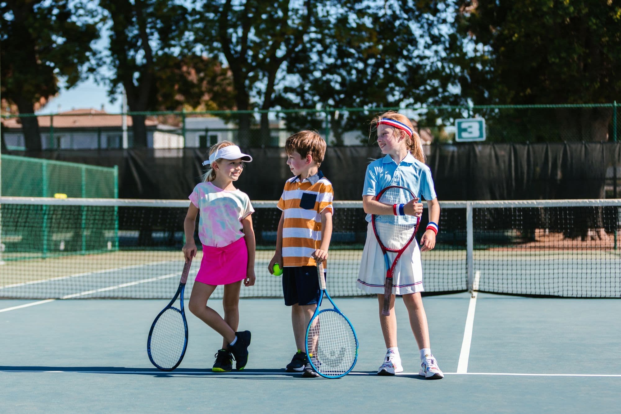 Three children with rackets at the net on a sunny court