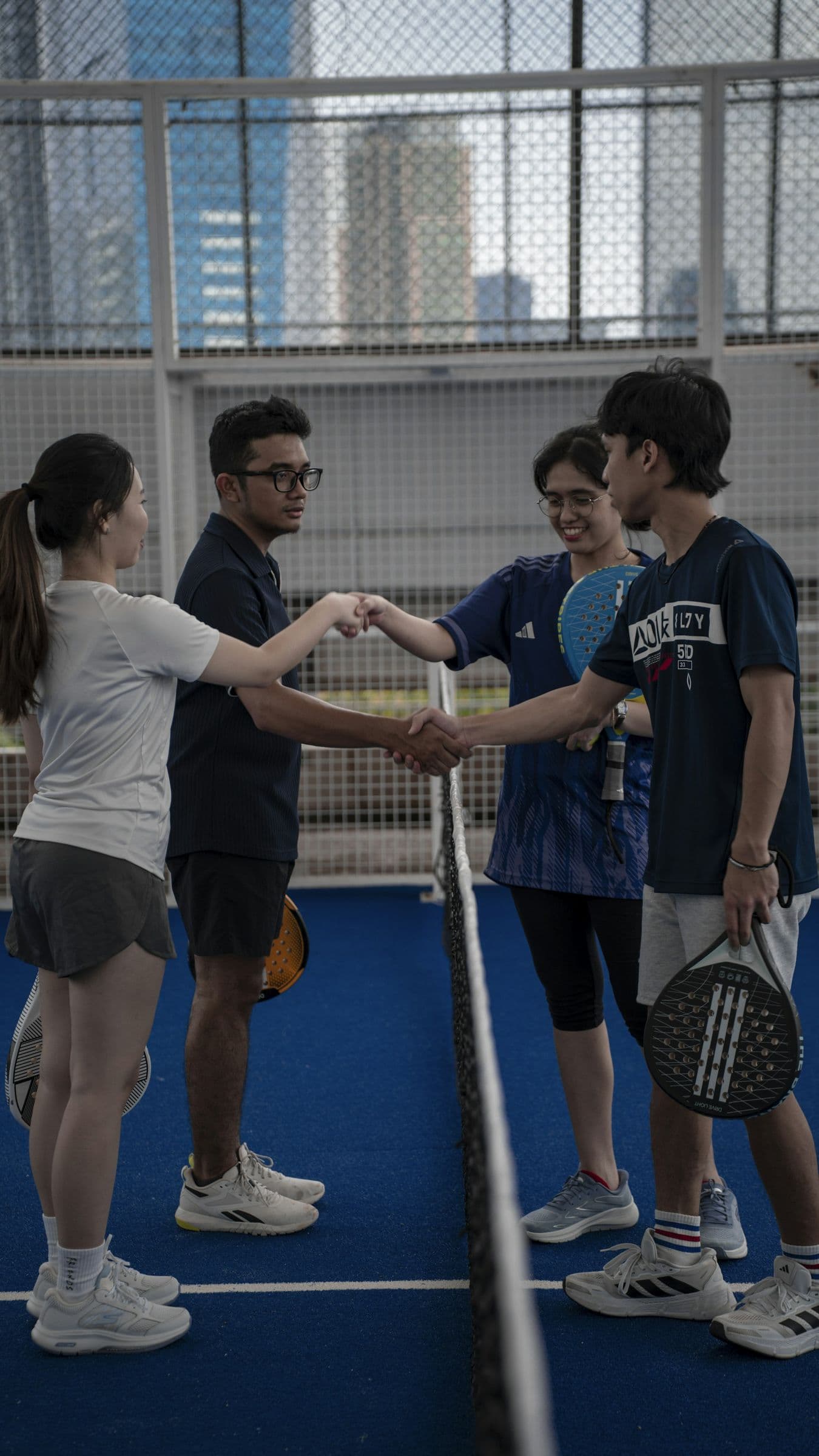Four friends shaking hands across the net after a game of padel