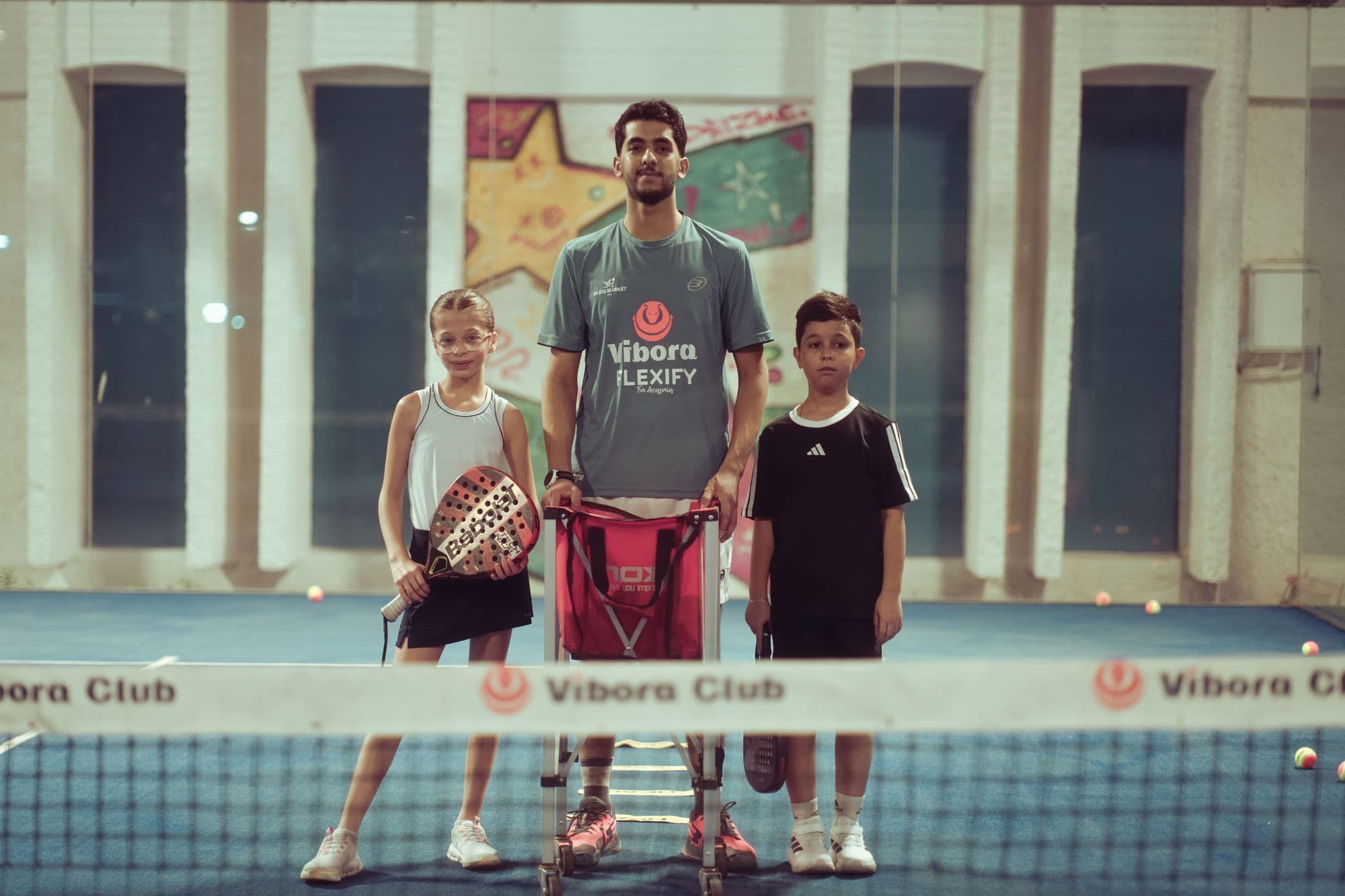 A padel coach with two children at the net