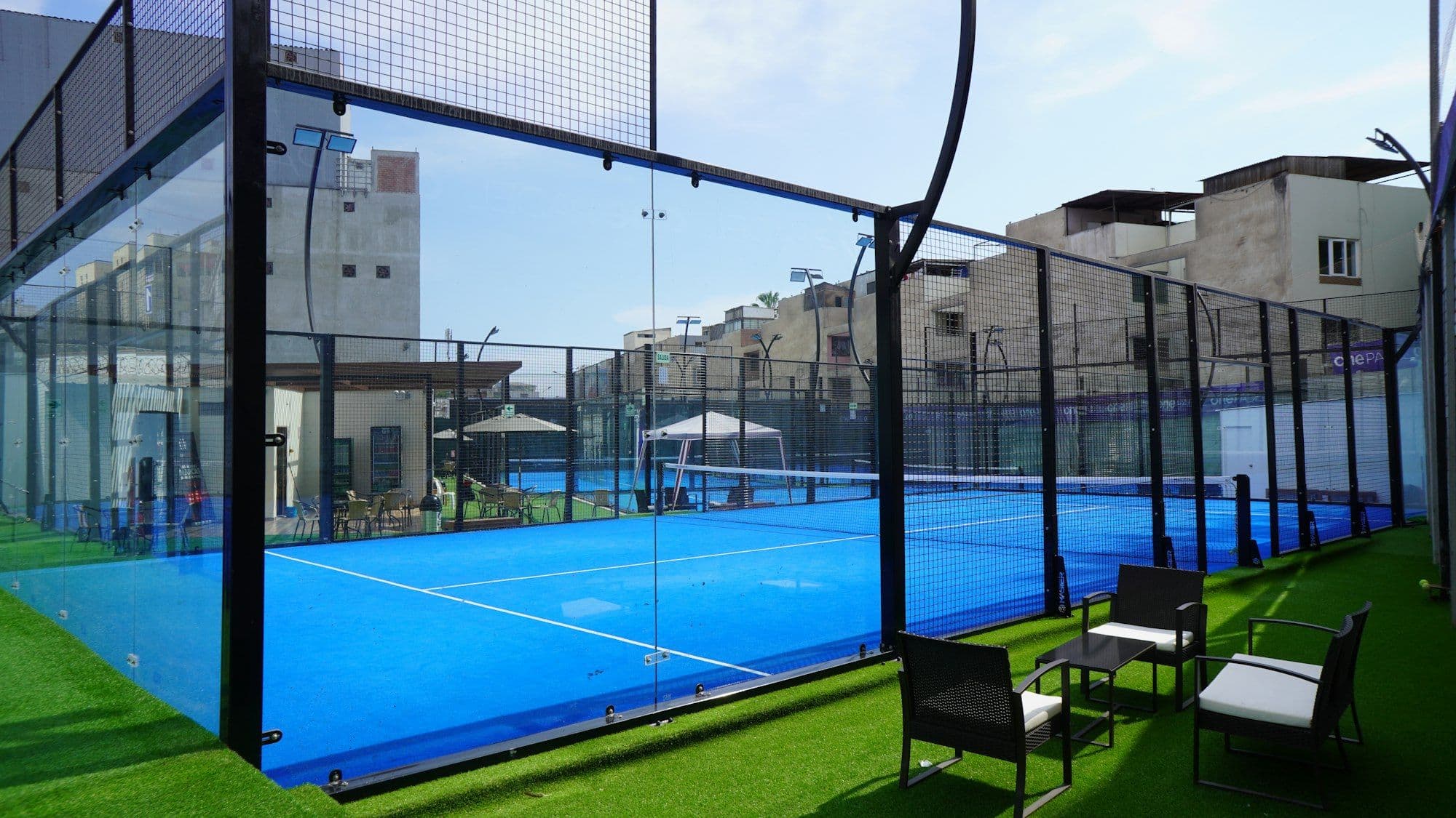 Glass padel courts beside a lawn on a sunny day
