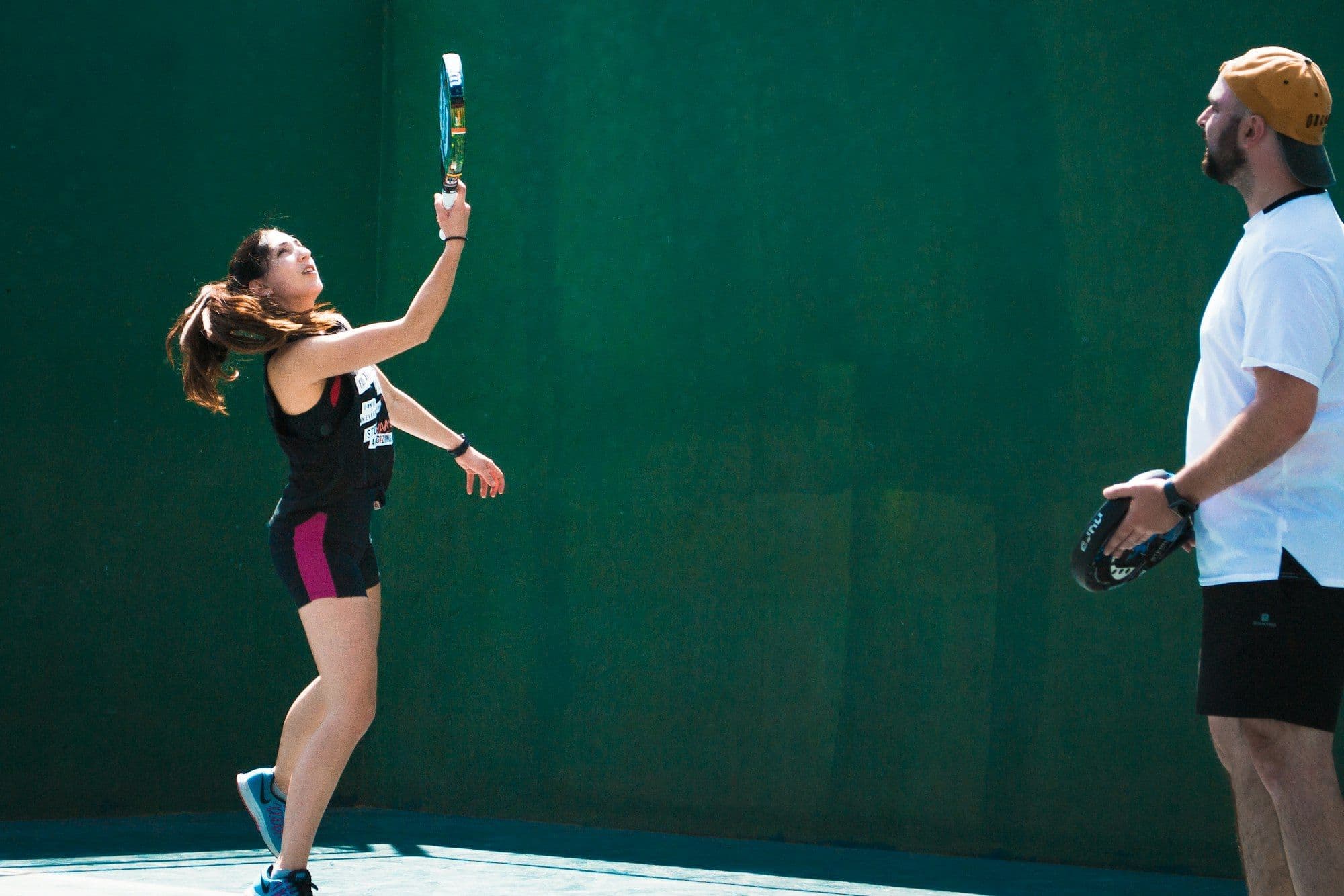 A padel coach watching a player practise her overhead