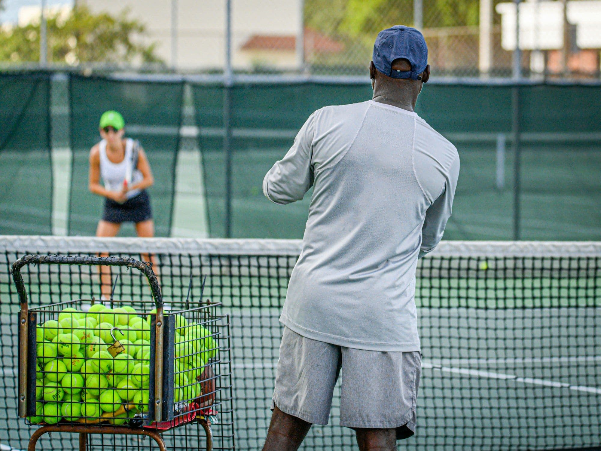 A tennis coach feeding balls from a basket during a lesson